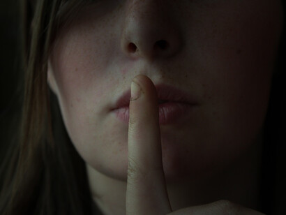 A woman with a finger in front of her mouth, silencing herself. Stop someone’s voice over some issues or some particular matter