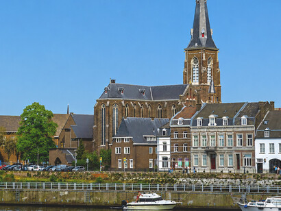 Maastricht, the Netherlands, Maastricht’s charming riverside lined with historic buildings and an iconic church beneath a bright summer sky