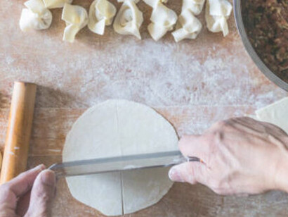 Hands skillfully open the manti, filling it with a generous portion of flavorful minced meat