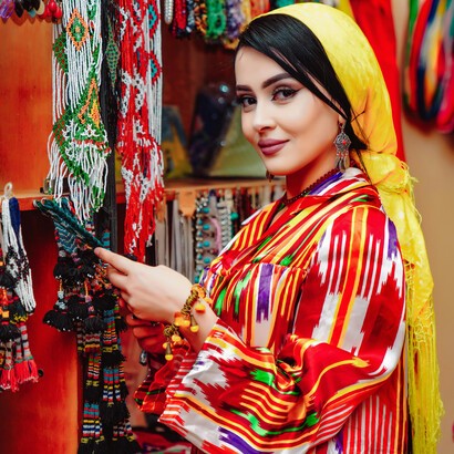A woman in Uzbekistan wearing a yellow scarf and holding a colorful round bag, representing traditional art and craftsmanship