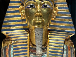 The golden funerary mask of Tutankhamun, featuring a striped nemes headdress and protective cobra and vulture symbols, at the Grand Egyptian Museum, Giza, Egypt