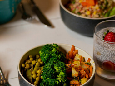 A colorful mix of sliced fruits, quinoa, and garden-fresh vegetables beautifully arranged in a black ceramic bowl, representing balanced and low-calorie nutrition
