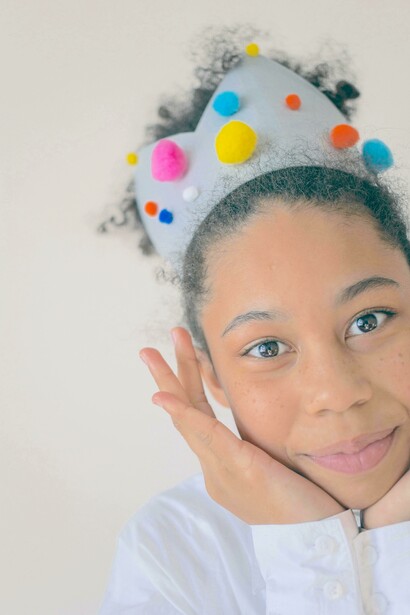 Menina negra positiva com coroa criativa tocando o rosto e sorrindo para a câmera