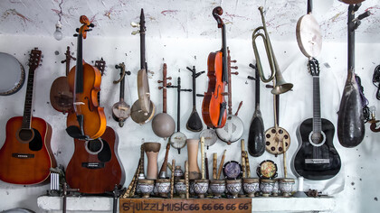 A variety of colorful guitars and other musical instruments, including violins, displayed on the wall