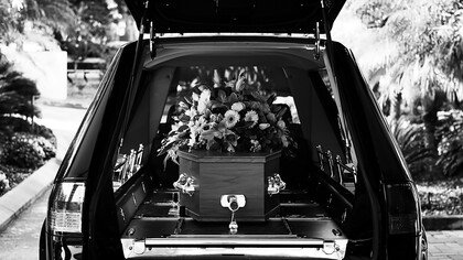 A grayscale photo of a car adorned with flowers, part of a solemn funeral procession