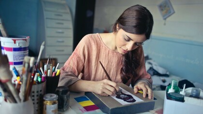 Woman painting a desk next to pots of paint and pencils