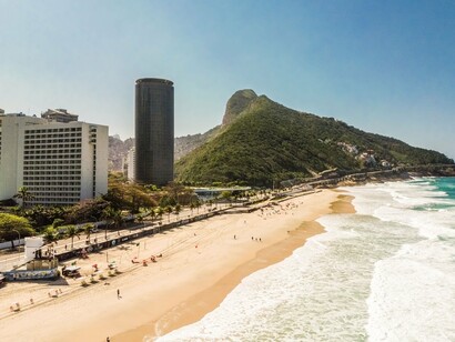 A aproximação do olhar evidencia a densidade da ocupação urbana junto à paisagem natural. A Pedra da Gávea e o relevo funcionam como elementos físicos que, na própria imagem, ajudam a perceber a separação entre territórios socialmente distintos