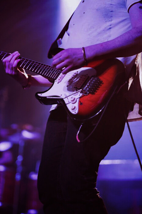 A man playing electric guitar under stage lights at a rock concert