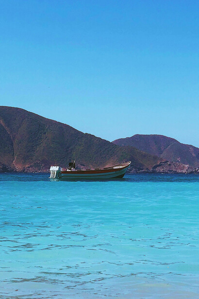 A boat in beautiful aqua waters with clear blue sky overhead, rolling hills deep in the distance