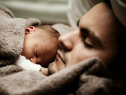 Un padre duerme junto a su bebé recién nacido