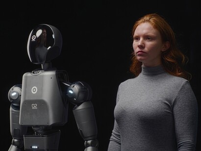 An advanced humanoid robot stands beside a young woman, highlighting the evolving relationship between humans and AI