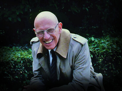 Michel Foucault sitting in front of a bush outside
