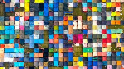 Vista aérea de tecidos coloridos secando ao ar livre em Dhaka, Bangladesh, mostrando práticas têxteis culturais. As diferentes cores e padrões criam uma composição visual que destaca a diversidade presente no universo têxtil. Durante séculos, a produção dessas tonalidades envolveu processos químicos e naturais que marcaram profundamente a relação entre moda, saúde e meio ambiente. Hoje, compreender a origem dos corantes e os impactos da indústria tornou-se parte essencial de um consumo mais consciente e sustentável