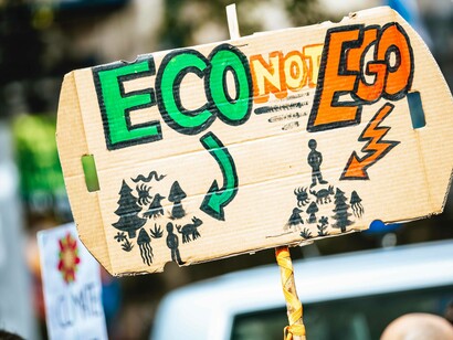 A sign that is on a stick for all to see reads "eco not ego" referencing the absolute necessity for climate action