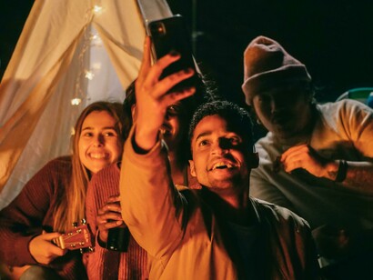 Friends around a campfire taking a selfie, representing how far we've come from pond reflections