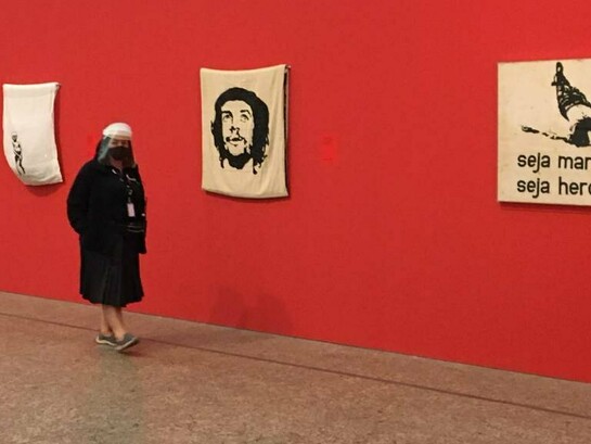 Visitante observa obras de Hélio Oiticica em exposição, entre elas a emblemática "Seja marginal seja herói". Inspirada na morte de Manuel Moreira, conhecido como "Cara de Cavalo", a criação tornou-se um manifesto artístico contra a violência e a exclusão, reafirmando a capacidade da arte de desafiar convenções — movimento que também marcou a literatura brasileira a partir da Geração de 45. Ao transformar um episódio de violência em reflexão artística, Oiticica ajudou a redefinir os caminhos da arte contemporânea brasileira, em sintonia com a renovação da literatura e de outras formas de expressão