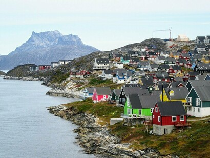 Casas coloridas acompanham a costa e avançam pelas encostas rochosas de Nuuk, diante das montanhas que cercam a cidade. A ocupação urbana convive diretamente com a paisagem natural que caracteriza a Groenlândia