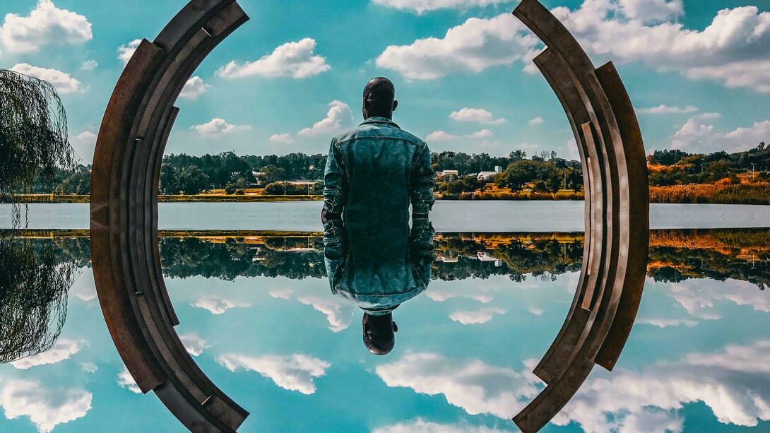 A man's self reflection, framed by a sculpture and the sky