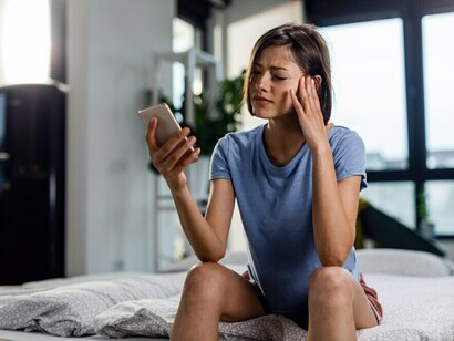 A stressed woman glances between her phone and the sky — caught between AI and memory