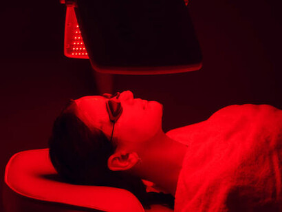 A young woman receiving red LED light therapy during a facial treatment at a beauty and wellness clinic