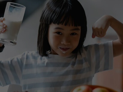 With a radiant smile, a cheerful little girl savors the goodness of milk while relishing a plate filled with vibrant and nutritious fresh foods, embodying the joy of a healthy and delightful meal