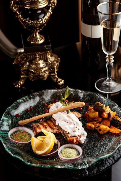 Side view of baked fish fillet garnished with vegetables, spices, and sauce on a plate, paired with a glass of white wine on the table