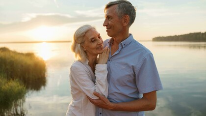 A sweet couple standing by the water at sunset, sharing a peaceful moment together