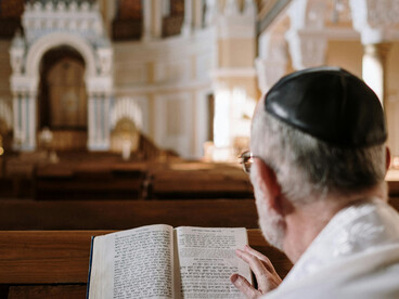 A man wearing a kippah prays quietly as he reads the Bible