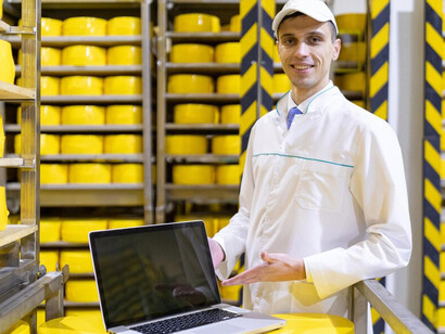A technologist holding a laptop stands in the dairy factory's production line, optimizing operations while focusing on food supply chain management, food traceability, and blockchain technology