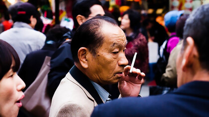 An elderly yakuza member smoking outside, his expression calm and contemplative