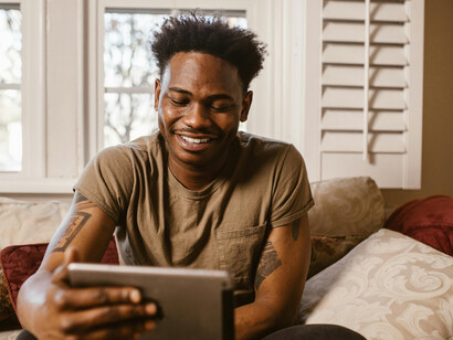 An emotional man sitting on a couch while looking at his tablet