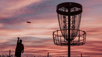 A silhouette of a man throwing a disc toward a disc golf basket