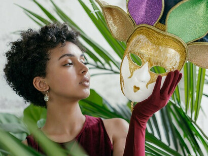 A woman holding an ornate mask before her face, representing the performance of perfection expected by society