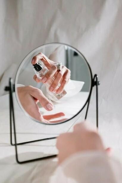 A woman puts perfume on her wrist as she rests her arm on white sheets