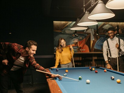 A group of friends focused on a pool table, representing the kind of leisure that restores rather than drains