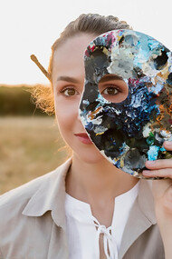 A creative young woman holding a painting palette, inspired by the connection between art and dreams, surrounded by surreal imagery