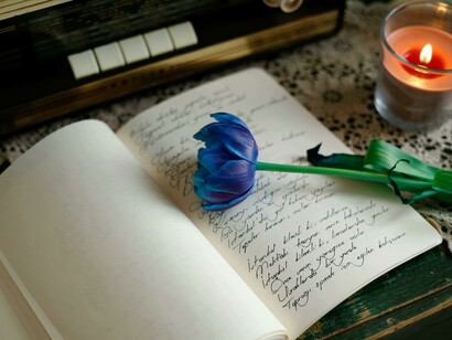A diary and a blue flower in candlelight, mirroring the tenderness of silent thoughts