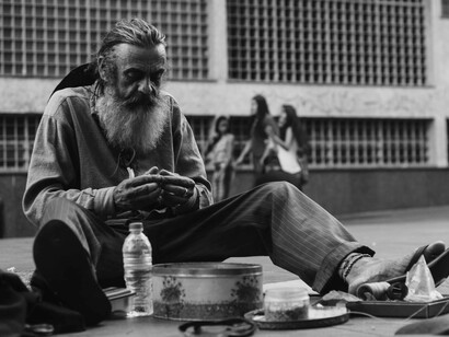A homeless man sitting on the ground with a bottle, eating