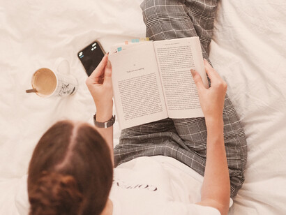 Mujer acostada en cama, disfruta de la lectura junto con un café