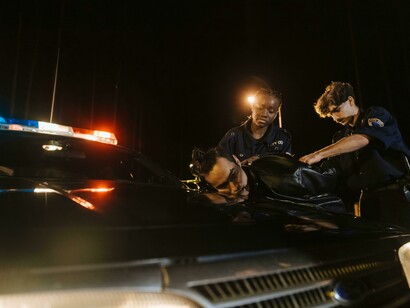 Police arrest in progress as an officer restrains a man against a police car