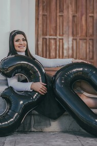 A woman sitting on the floor with balloons, celebrating her 30th birthday