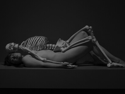 A nude individual reclining beneath a skeleton, an artwork by Marina Abramović, photographed by Jonathan Muzikar
