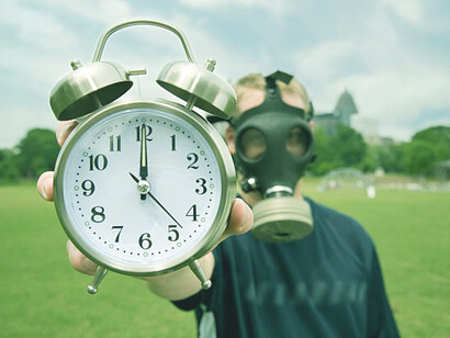 A man wearing a nuclear mask and holding a Doomsday Clock, symbolizing the nuclear threat and the impact of climate change