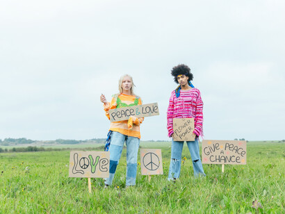 A man and a woman hold and are surrounded by signs of peace and love, in a field