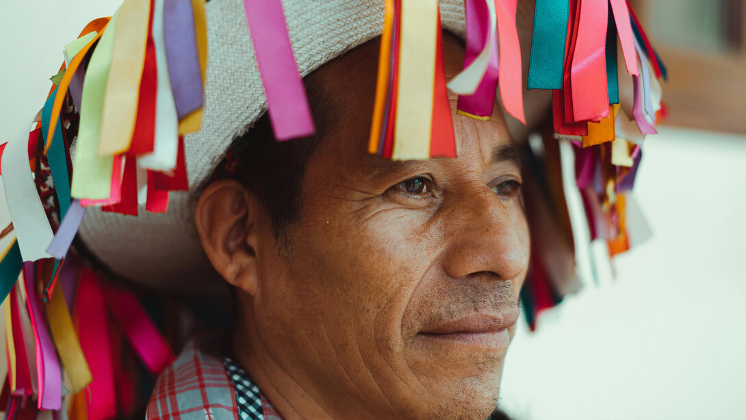 A Native American middle-aged man wearing a colourfuly adorned hat, looking into the distance