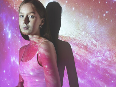 A young woman immersed in a universe texture projection embodies the essence of feminine energy, reflecting its transformative power and cosmic significance