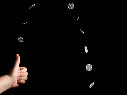 A hand tossing a coin, capturing the chance between global ruin and renewal