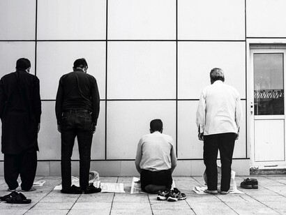 Muslim men praying as immigrants in their western adopted land and using newspapers as a prayer mat