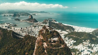 Vista aérea do Rio de Janeiro. Muito antes da chegada dos portugueses, a região da Baía de Guanabara já era habitada por povos indígenas, especialmente do tronco Tupi-Guarani. Os Tupinambás e os Tamoios viviam da pesca, da caça, do cultivo de mandioca e da coleta de frutos, em um sistema de vida baseado na relação com a natureza. Esses povos chamavam a região de “Guanabara”, que significa “seio do mar” em tupi, em referência à entrada da baía que hoje abriga a cidade. Era uma área estratégica por suas condições naturais de abrigo e abundância de recursos