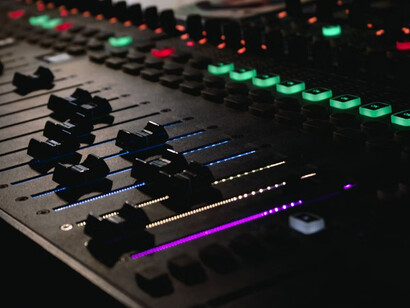 An analog sound board with numerous knobs is paired with AI music generation tools, illustrating the intersection of classic audio engineering and artificial intelligence